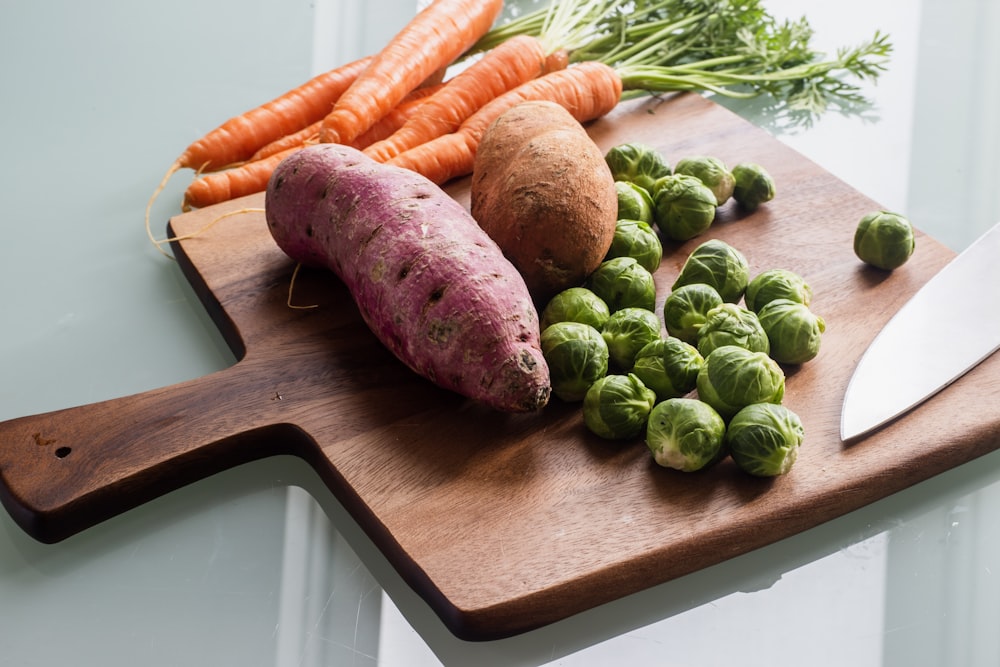 carrots and green round fruits on brown wooden chopping board