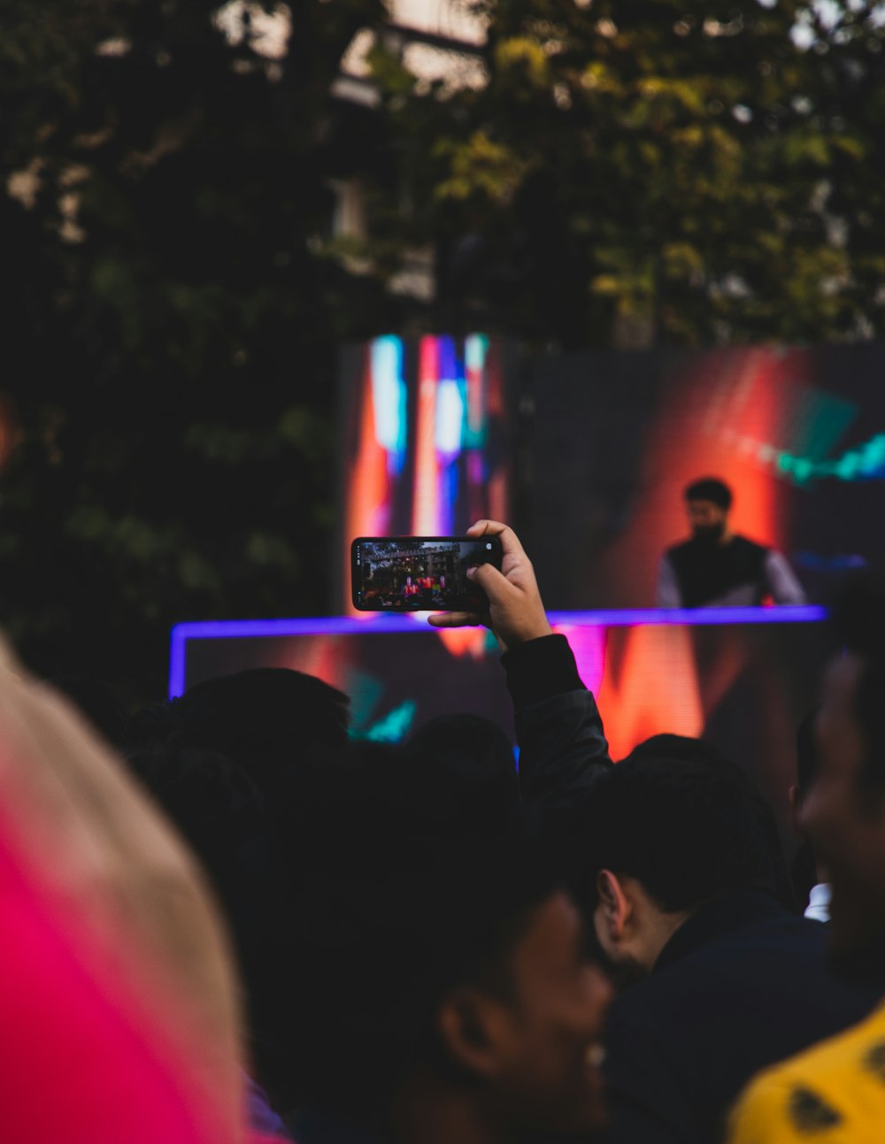 person holding smartphone taking photo of people in concert during night time
