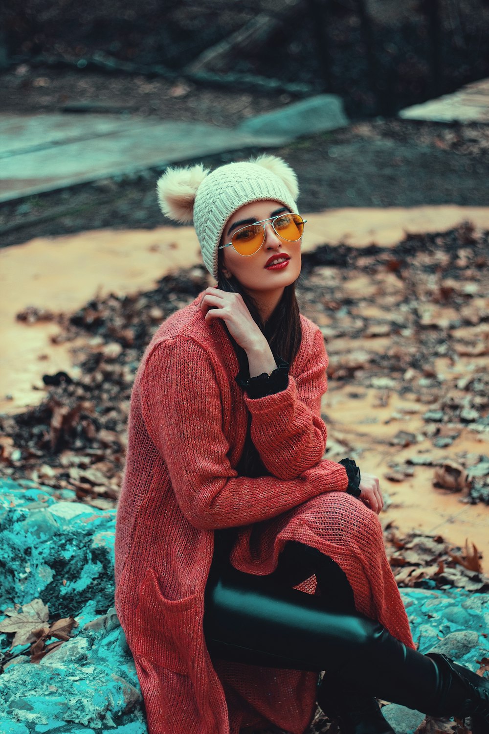 woman in red sweater and white knit cap sitting on rock during daytime