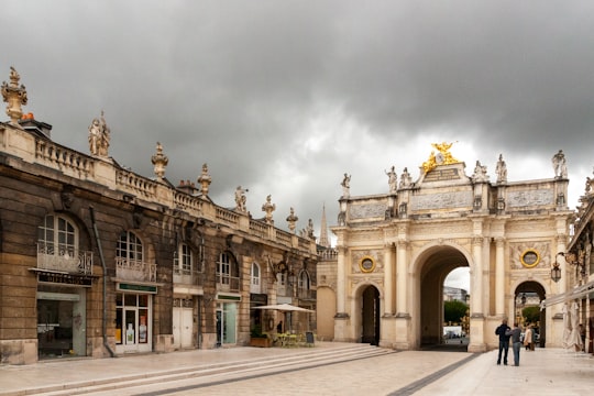 people walking on sidewalk near brown concrete building under white clouds during daytime in Arc Héré France