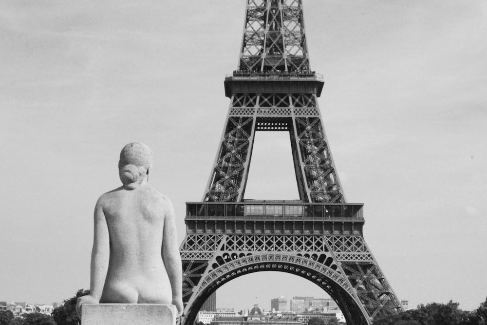 topless man standing near eiffel tower in grayscale photography