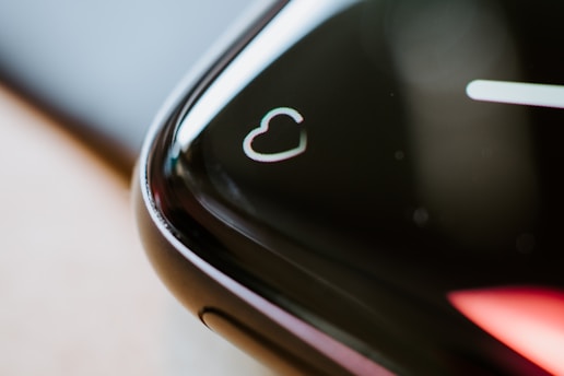 A close-up of the edge of a black smartwatch screen featuring a heart symbol, suggesting a focus on heart rate monitoring. The screen's curved edge reflects light, creating a sleek and modern appearance.