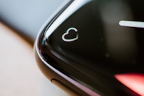 A close-up of the edge of a black smartwatch screen featuring a heart symbol, suggesting a focus on heart rate monitoring. The screen's curved edge reflects light, creating a sleek and modern appearance.