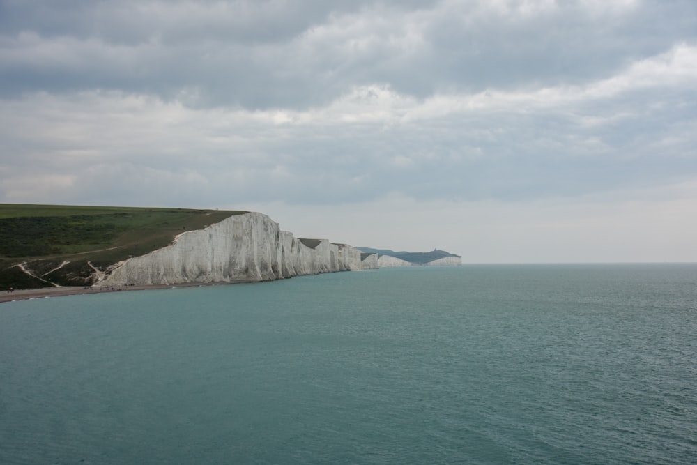 green and white mountain beside body of water under white clouds during daytime