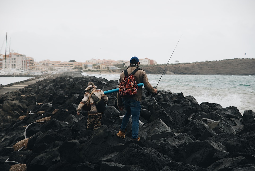 man in blue denim jeans and blue backpack standing on rocky shore during daytime