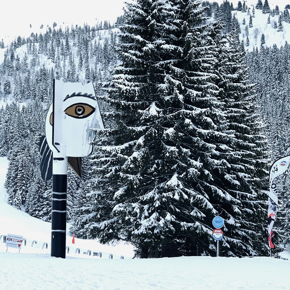 white and black snowman on snow covered ground near green pine trees during daytime