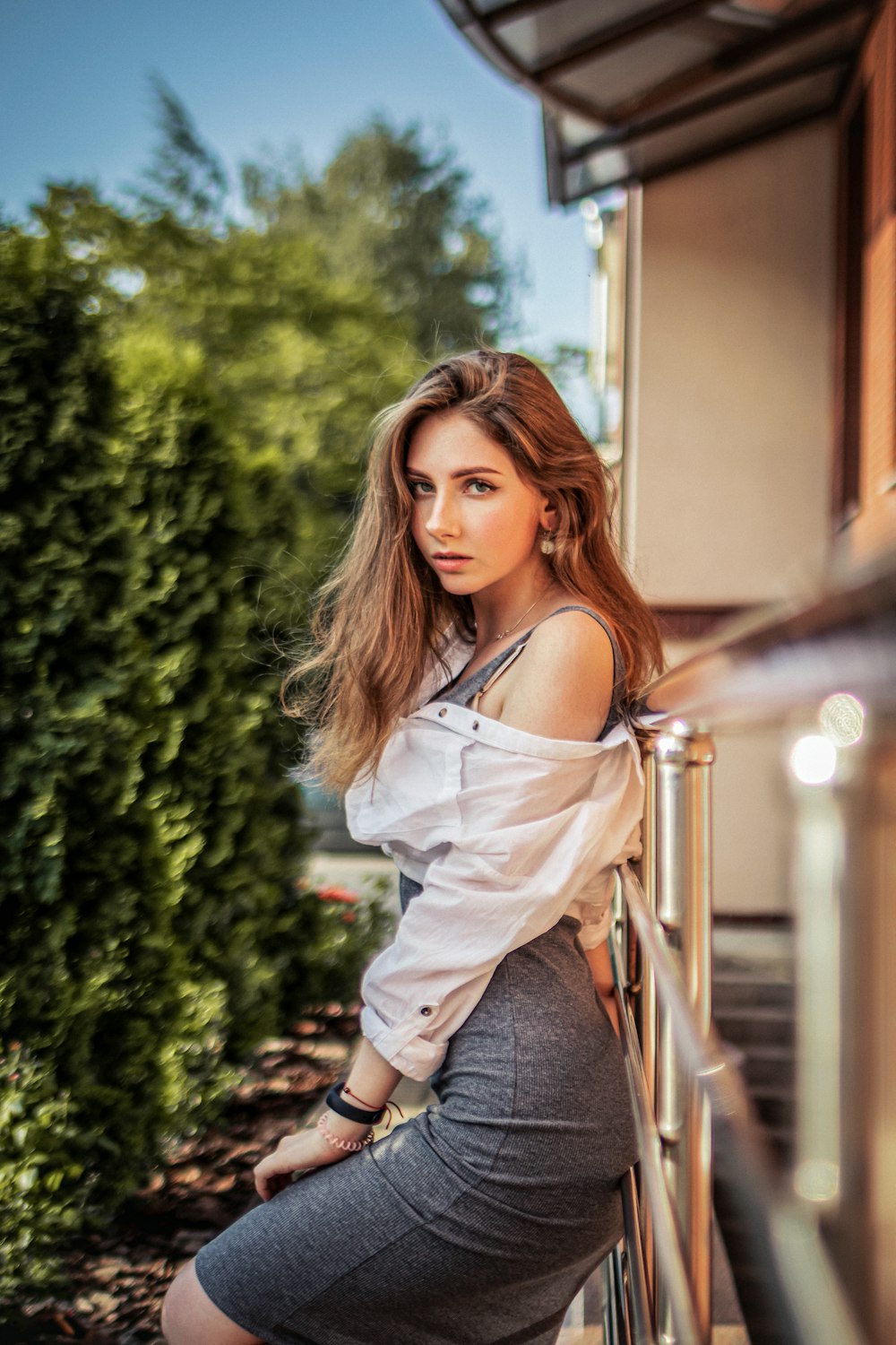 Femme en chemise blanche à manches longues et pantalon gris debout près de plantes vertes pendant la journée