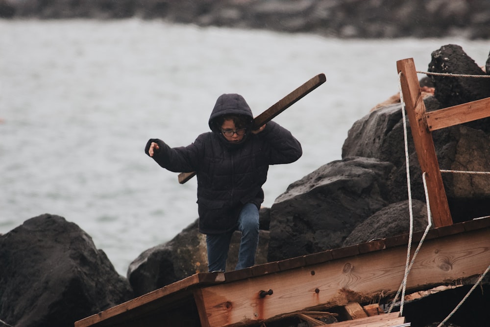 man in black jacket and blue denim jeans holding brown wooden stick