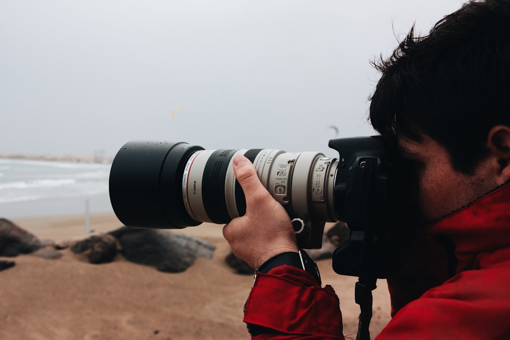 man in red jacket holding black dslr camera