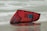 A red and black kiteboarding kite rests on a sandy beach with ocean waves in the background. The kite is partially wet, reflecting some light from the overcast sky.