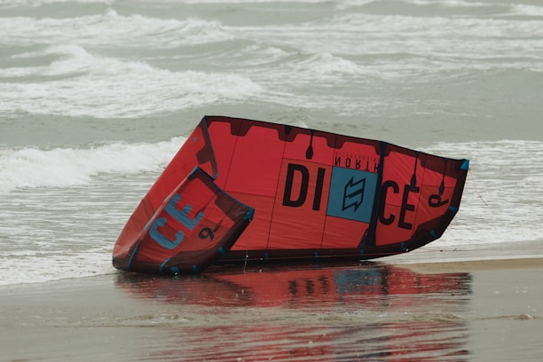 Close-up of colorful kiteboarding gear laid out neatly on a sandy beach with the Columbia River Gorge cliffs in the background.