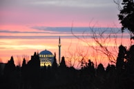 A peaceful sunset behind a mosque dome with minarets silhouetted.