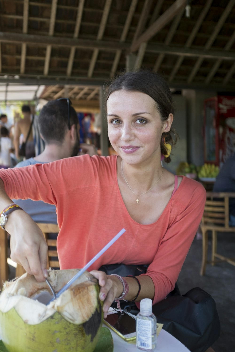 a woman sitting at a table cutting into a coconut