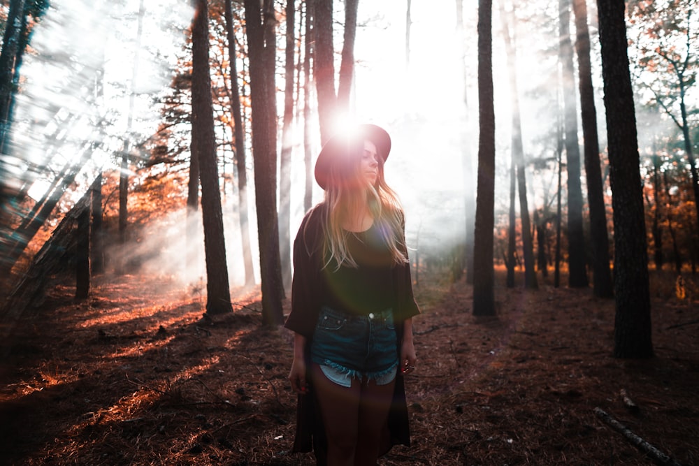 woman in green tank top and blue denim shorts standing in the woods during daytime