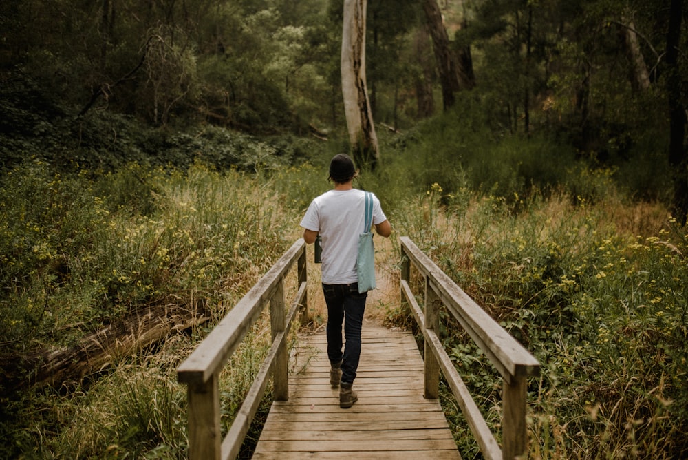 man in white shirt walking on wooden bridge