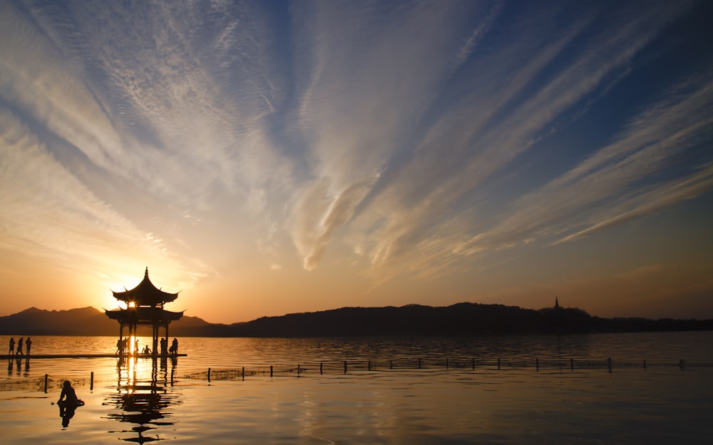 silhouette of house on water during sunset