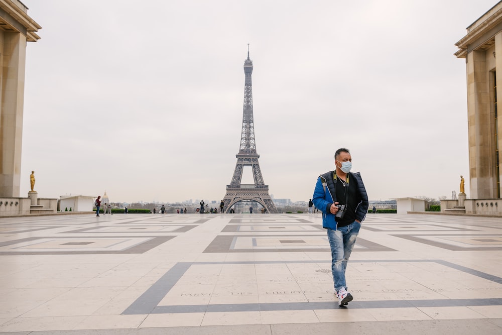 검은 재킷과 파란색 데님 청바지를 입은 남자가 에펠탑 근처의 회색 콘크리트 바닥에 서 있다