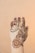 A hand decorated with intricate henna designs, featuring floral and paisley patterns. A red gemstone ring adorns one of the fingers, and a chain-like design adds elegance to the artwork. The background is a soft beige color, which highlights the detailed mehndi art.
