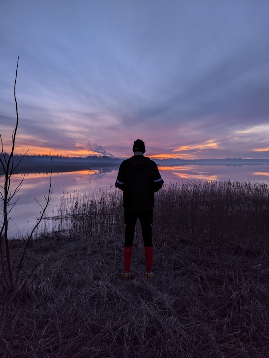 man in black jacket standing on grass field near lake during sunset in Riga Latvia