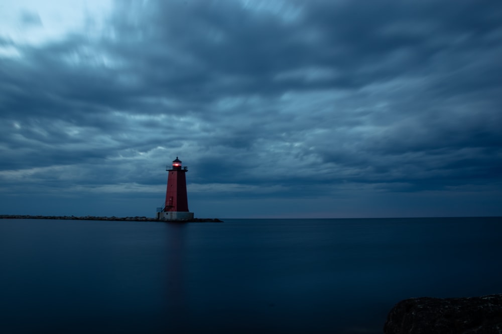 red and white lighthouse on the sea under gray clouds