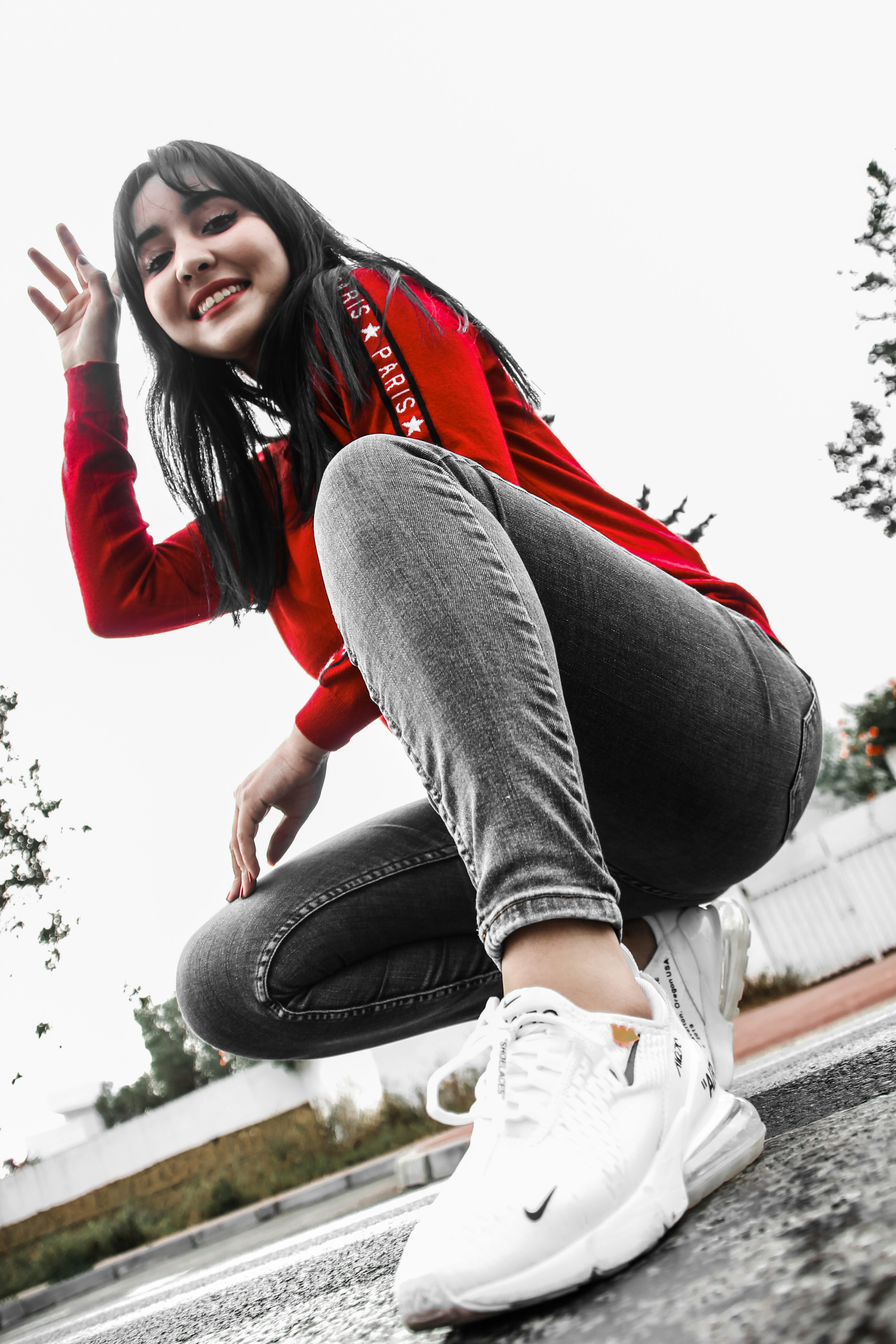 Wanita dengan jaket merah dan jeans denim biru duduk di bangku beton di siang hari