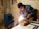 A person wearing protective goggles and gloves is engaged in welding a metal pipe on a workbench, surrounded by sparks. The scene takes place in a dimly lit workshop with raw walls and visible utility equipment.