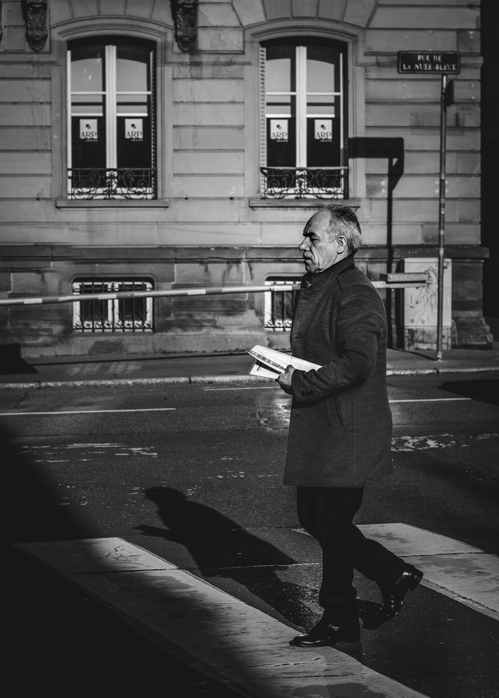 grayscale photo of woman in coat standing on sidewalk