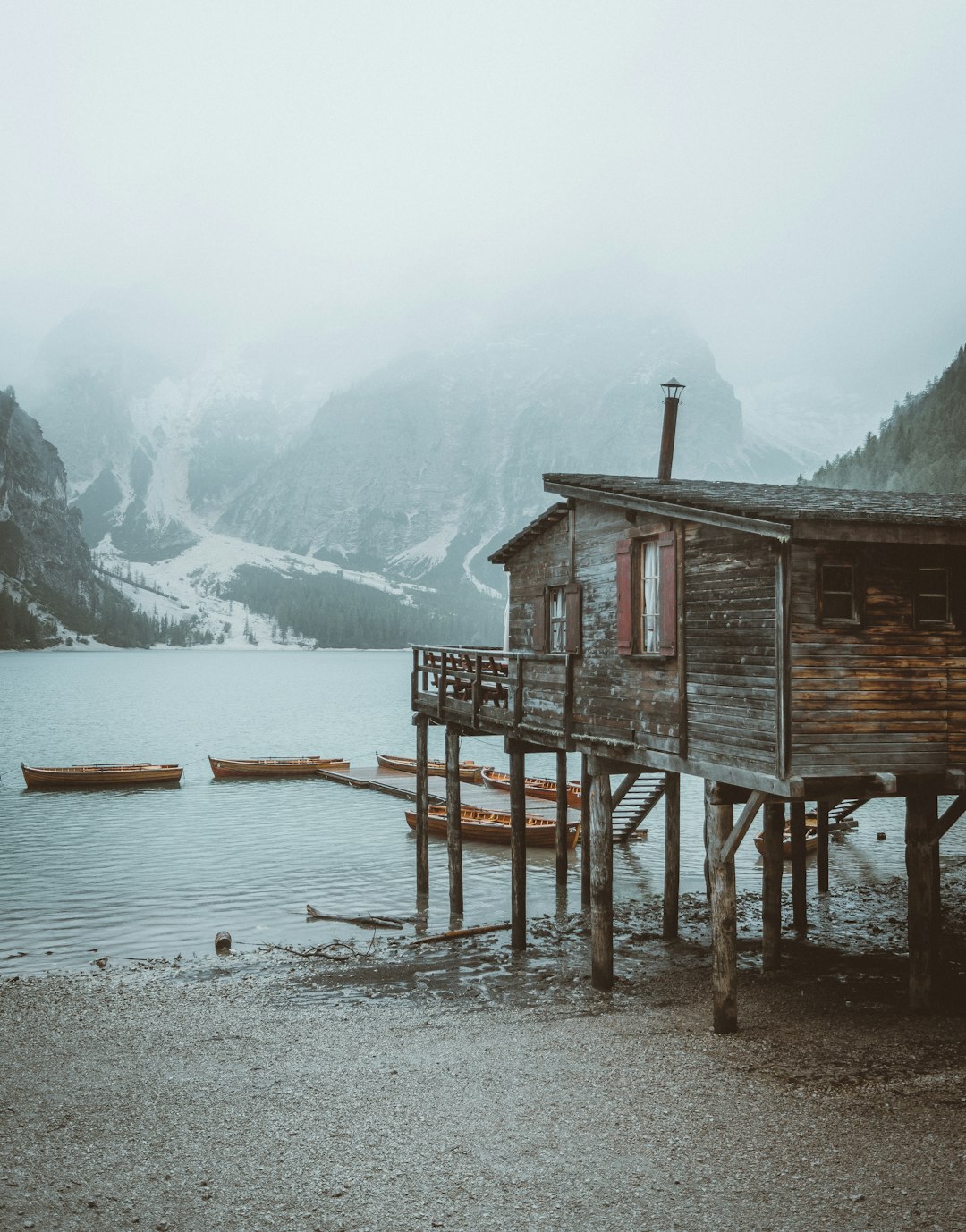 brown wooden house on body of water near snow covered mountain during daytime