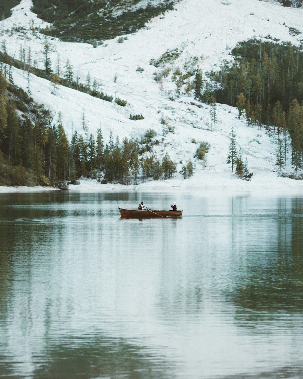 brown boat on lake near snow covered mountain during daytime
