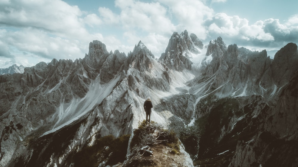 person standing on rocky mountain under white clouds during daytime