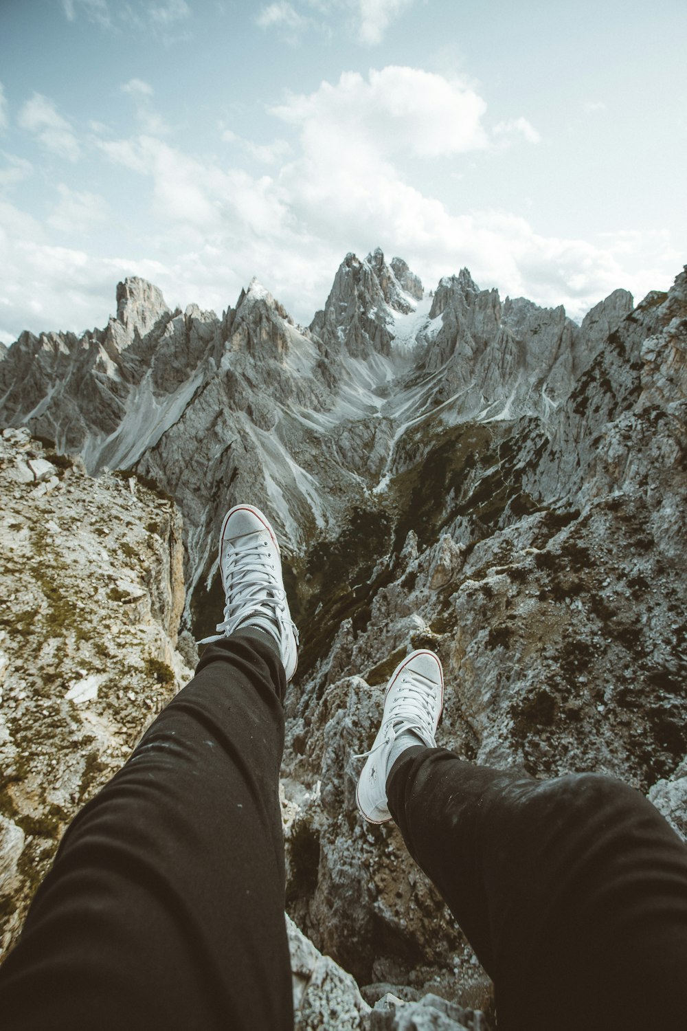 person in black pants and white sneakers sitting on rocky mountain during daytime