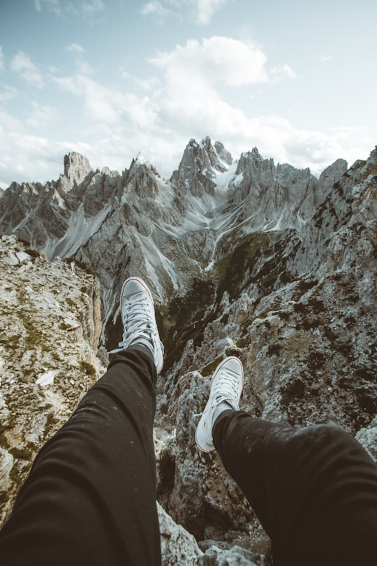 person in black pants and white sneakers sitting on rocky mountain during daytime in Tre Cime di Lavaredo Italy
