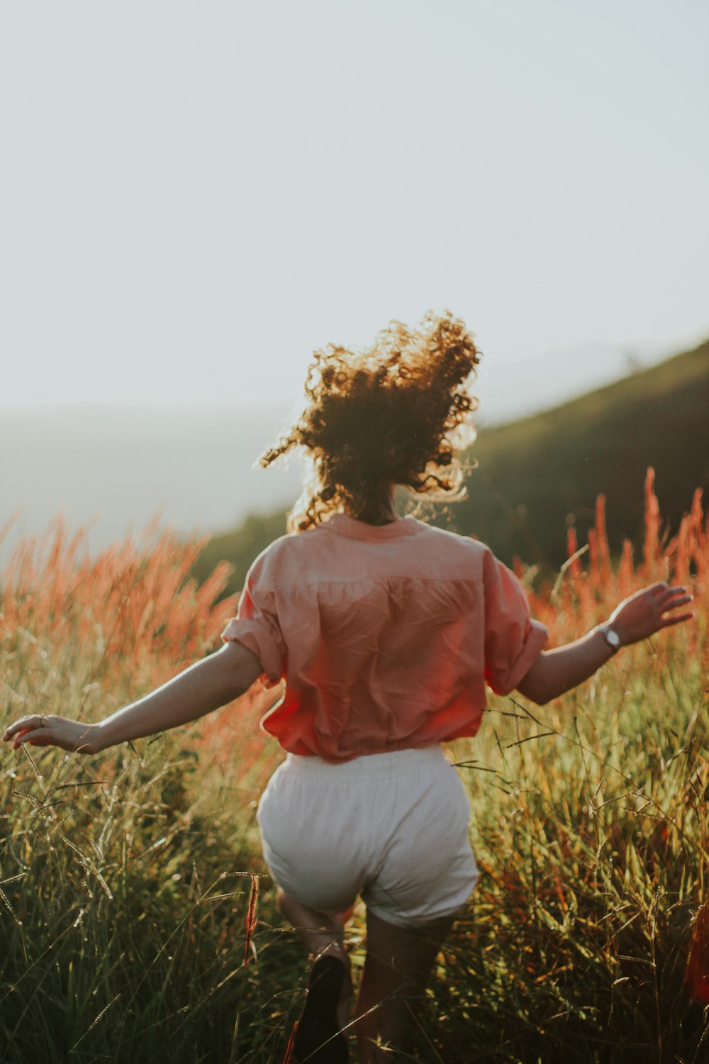 woman in pink long sleeve shirt and white pants standing on green grass field during daytime