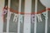 Colorful letters spell out 'PARABÉNS' strung together on a bright orange garland, displayed against a white paneled background.