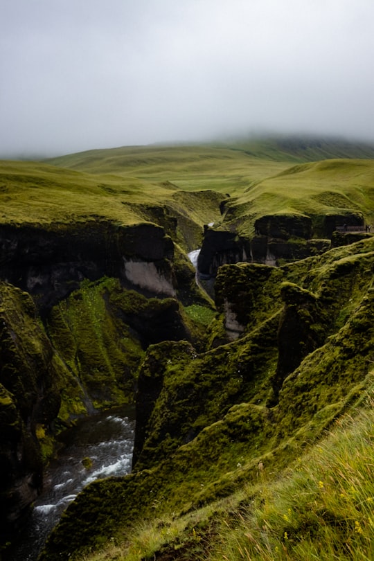 green and gray rocky mountain under gray sky in Fjaðrárgljúfur Iceland