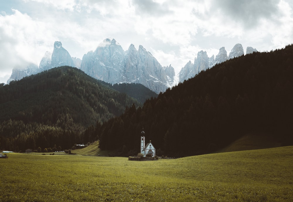 white concrete building on green grass field near mountains under white clouds during daytime