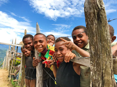 Children playing joyfully near a charcoal-colored rustic fence with warm sunlight filtering through.