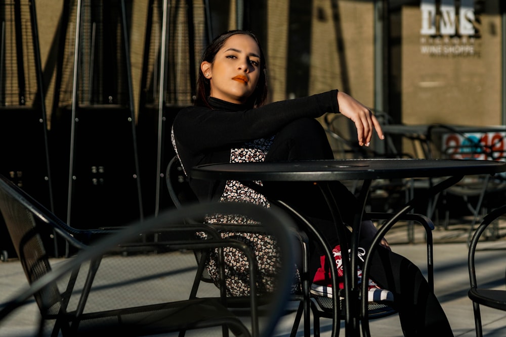 Donna in camicia nera a maniche lunghe seduta sulla sedia in metallo nero