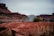 A camping scene set in a desert landscape features a small tent pitched on red rocky terrain. In the background, there are large rock formations and a wide, open sky. A bicycle is parked on the ground next to the tent, indicating a possible bike tour or adventure trip.