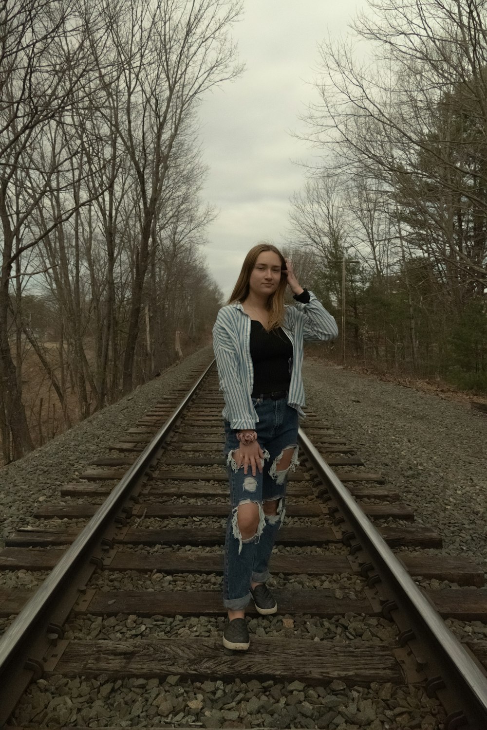 woman in white jacket and blue denim jeans standing on train rail during daytime