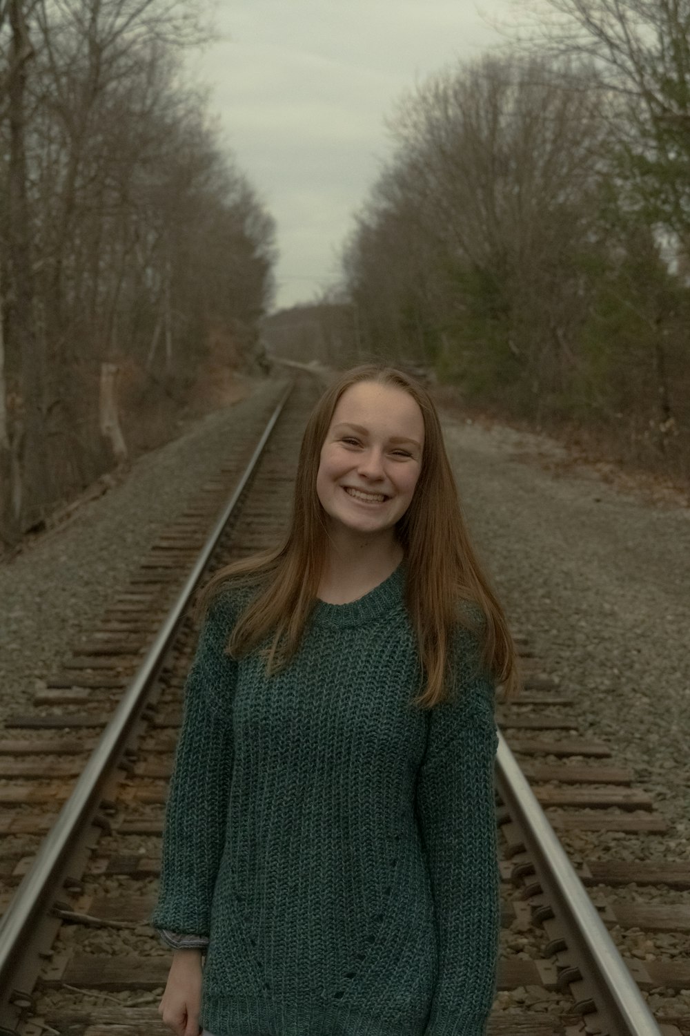 woman in gray sweater standing on train rail during daytime