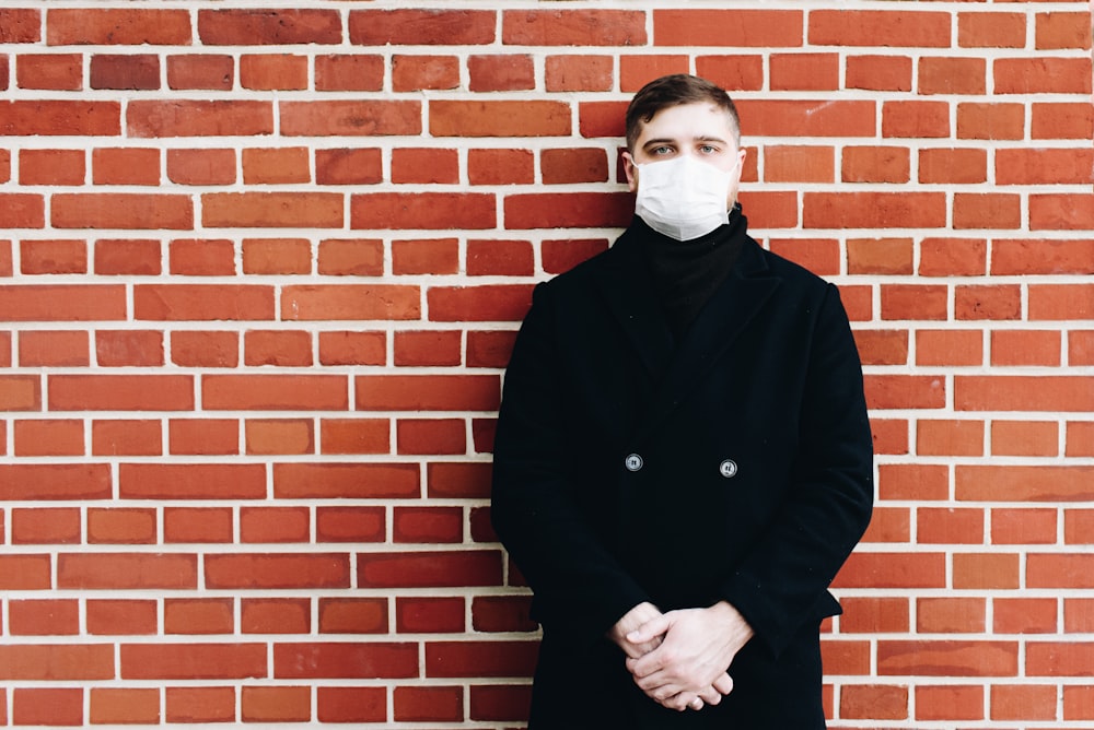 man in black coat standing beside brown brick wall