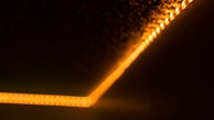 A diagonal line of warm, orange LED lights runs along a dark surface, creating a glowing effect that fades into the surrounding blackness. The lights appear to be in a strip form, subtly illuminating the area around them.