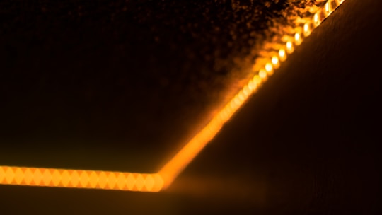 A diagonal line of warm, orange LED lights runs along a dark surface, creating a glowing effect that fades into the surrounding blackness. The lights appear to be in a strip form, subtly illuminating the area around them.