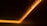 A diagonal line of warm, orange LED lights runs along a dark surface, creating a glowing effect that fades into the surrounding blackness. The lights appear to be in a strip form, subtly illuminating the area around them.