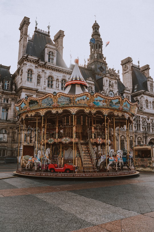 people riding on carousel in front of white concrete building during daytime in Hôtel de Ville France