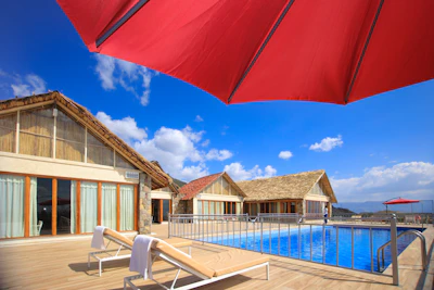 A row of comfortable sun loungers with beige cushions beside the calm central pool under soft sunlight.
