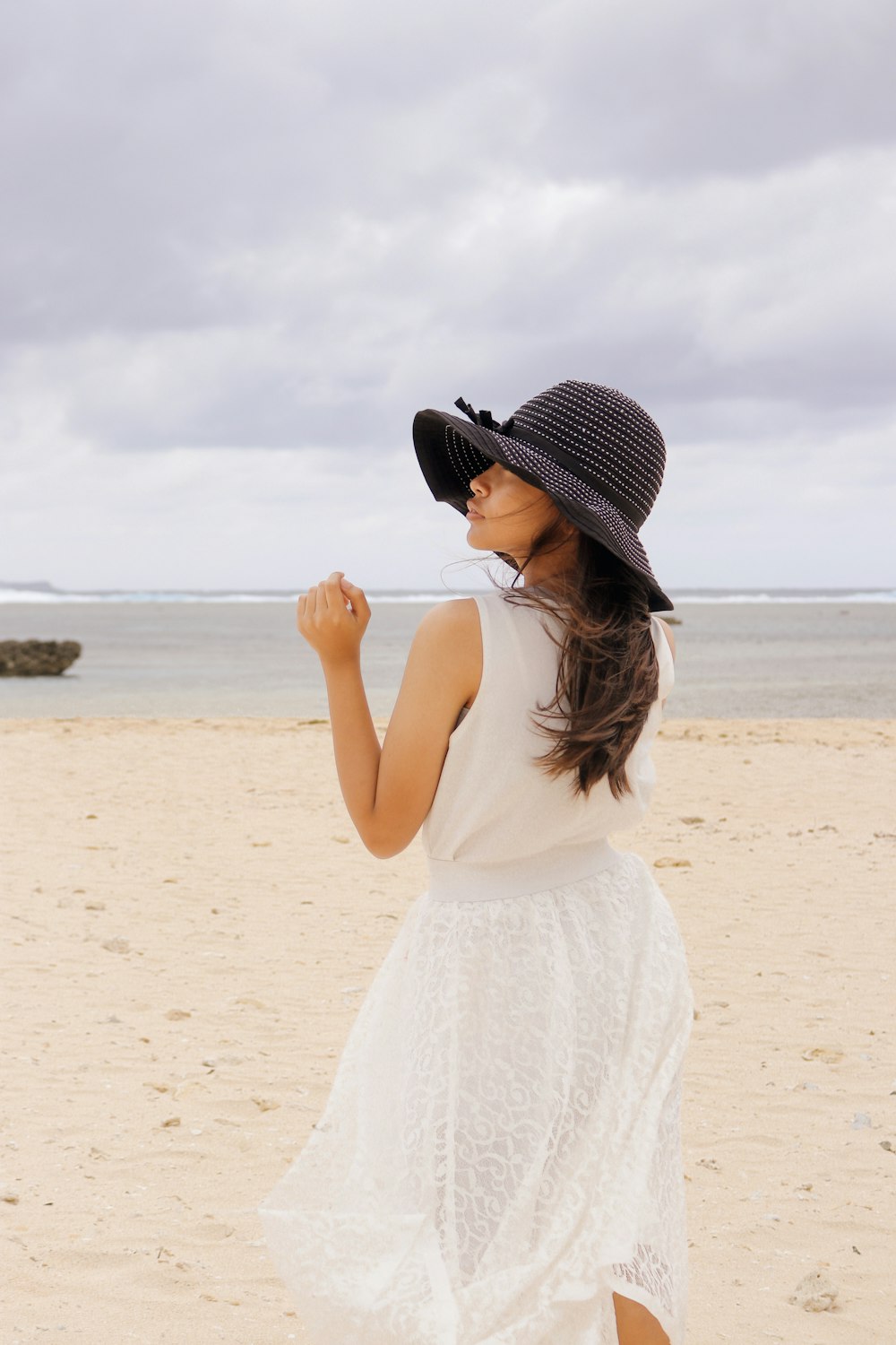 woman in white tank top and white skirt standing on beach during daytime