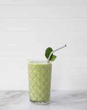 A glass of green smoothie topped with fresh berries and seeds on a kitchen counter.