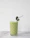 Close-up photo of a smiling woman holding a glass of green smoothie in a cozy kitchen.